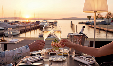 Ausblick auf den See und zwei Hände, die mit Champagnergläsern anstossen