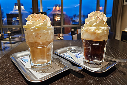 Bar table with two hot drinks with cream topping and some alcohol