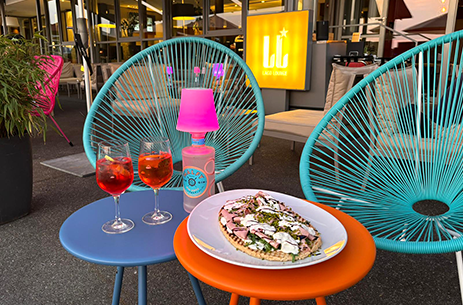 Bunte Terrassenbestuhlung der Lago Lounge mit zwei Spritzgetränken und einem Bruschettone