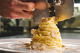 Tagliolini mit Trüffelsauce, sichtbar ist eine Hand, die Trüffel über das Gericht reibt